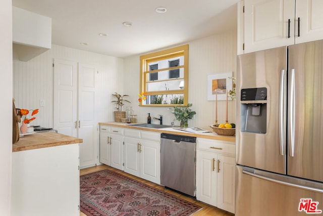 kitchen featuring wood counters, sink, light wood-type flooring, appliances with stainless steel finishes, and white cabinets