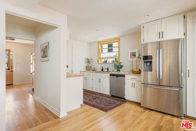 kitchen with stainless steel appliances, white cabinetry, and light wood-type flooring