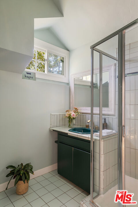 bathroom with walk in shower, vanity, tile patterned flooring, and vaulted ceiling