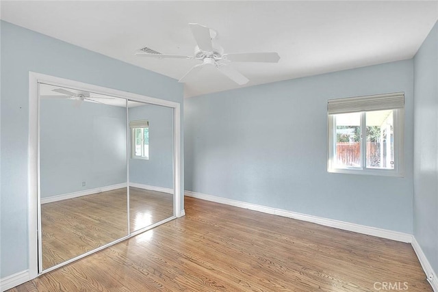 unfurnished bedroom featuring ceiling fan, a closet, multiple windows, and light wood-type flooring