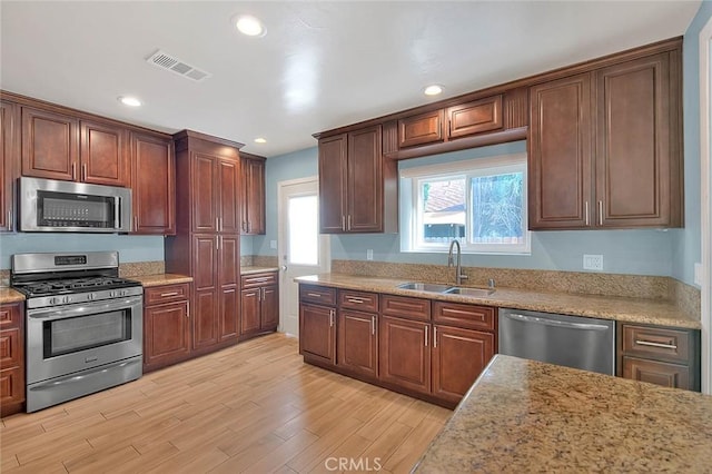 kitchen featuring appliances with stainless steel finishes, sink, light stone counters, and light hardwood / wood-style flooring