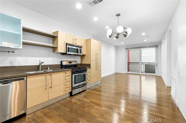 kitchen with light brown cabinetry, dark countertops, a sink, stainless steel appliances, and visible vents