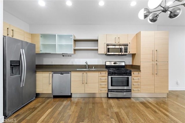 kitchen featuring dark wood-style flooring, light brown cabinetry, dark countertops, a sink, and stainless steel appliances