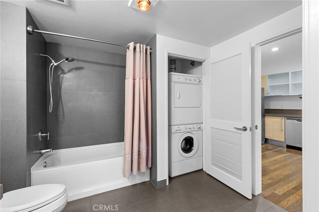 bathroom featuring toilet, stacked washing maching and dryer, shower / tub combo, and hardwood / wood-style flooring