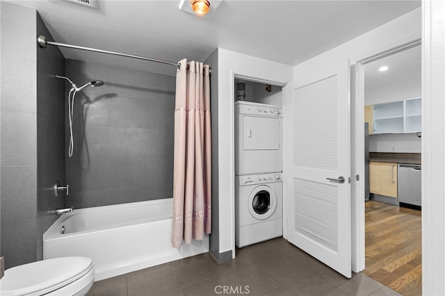 bathroom featuring shower / bath combo with shower curtain, tile patterned floors, stacked washer / dryer, and toilet