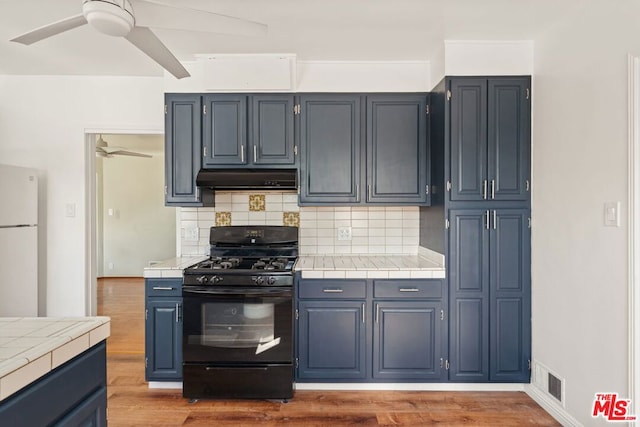 kitchen featuring tile countertops, backsplash, white fridge, ceiling fan, and black gas range