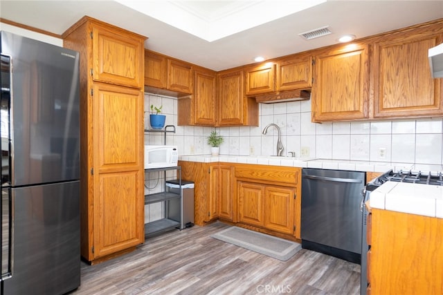 kitchen featuring tile countertops, sink, decorative backsplash, light hardwood / wood-style floors, and stainless steel appliances