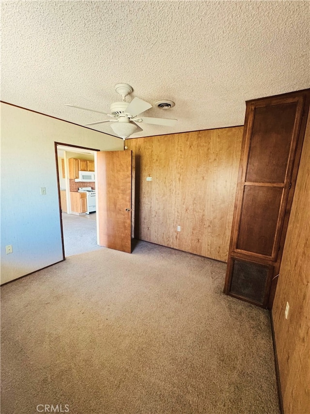 spare room featuring ceiling fan, wooden walls, light carpet, and a textured ceiling