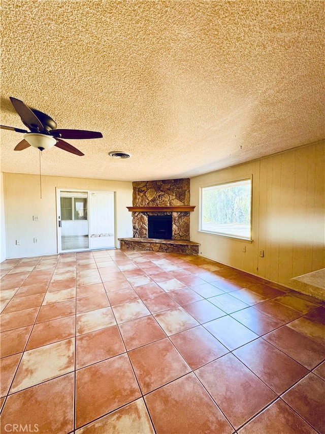 unfurnished living room featuring ceiling fan, a fireplace, tile patterned flooring, and a textured ceiling