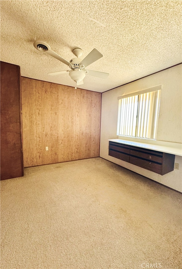 spare room with ceiling fan, wooden walls, carpet floors, and a textured ceiling