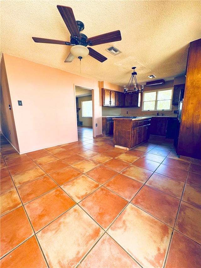 kitchen featuring ceiling fan, hanging light fixtures, a center island, a textured ceiling, and tile patterned floors