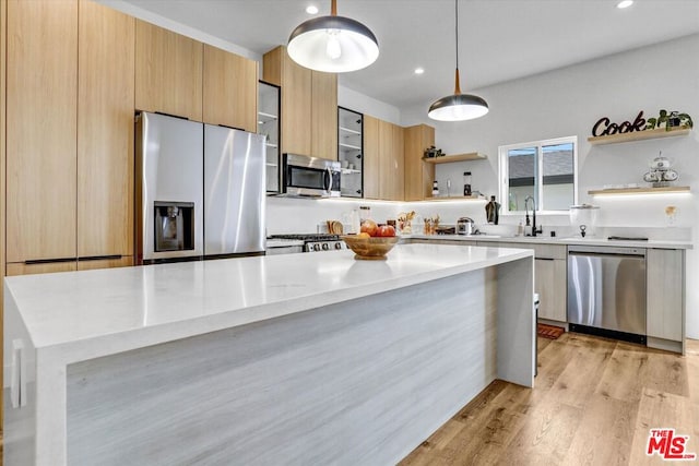 kitchen with sink, light stone counters, hanging light fixtures, light hardwood / wood-style flooring, and appliances with stainless steel finishes