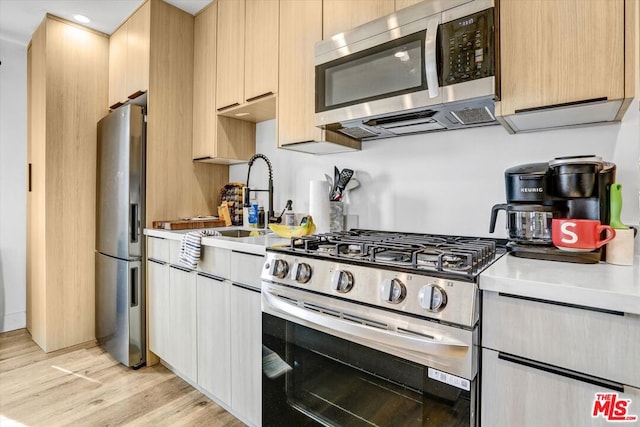 kitchen with appliances with stainless steel finishes, sink, light brown cabinetry, and light wood-type flooring