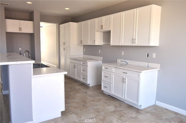 kitchen with white cabinetry, sink, light stone counters, and a center island