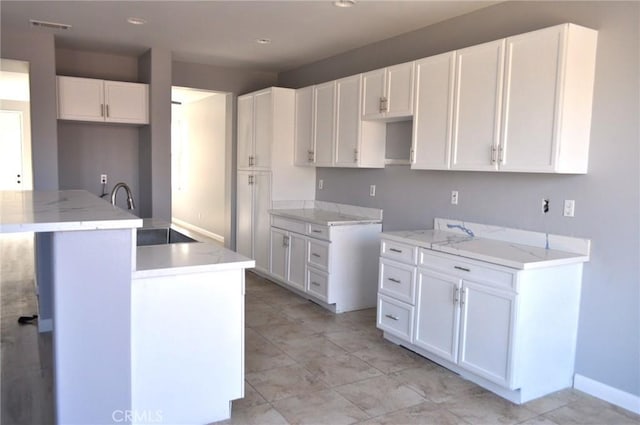 kitchen with light stone counters, sink, a center island, and white cabinets