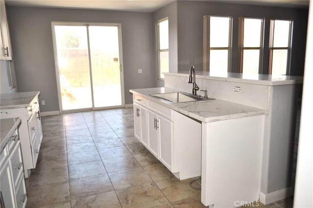 kitchen with light stone counters, a center island, sink, and white cabinets