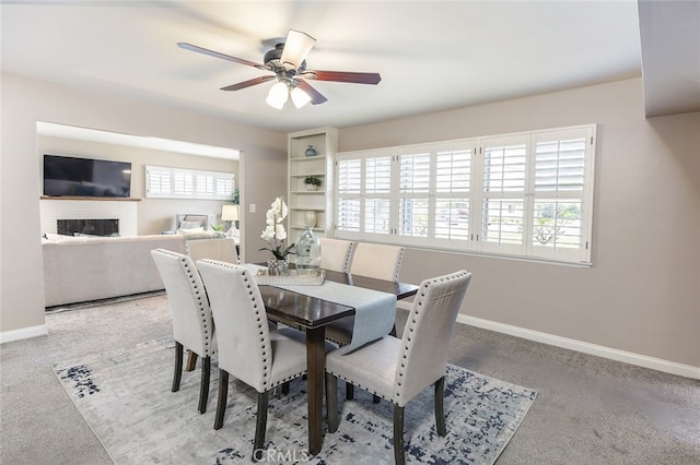 dining room featuring ceiling fan, a fireplace, a healthy amount of sunlight, and carpet flooring