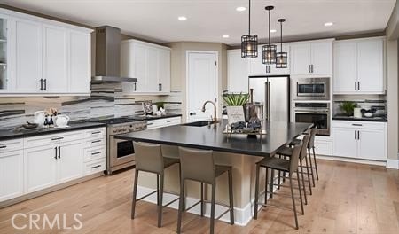 kitchen with wall chimney exhaust hood, sink, a center island with sink, high quality appliances, and white cabinets