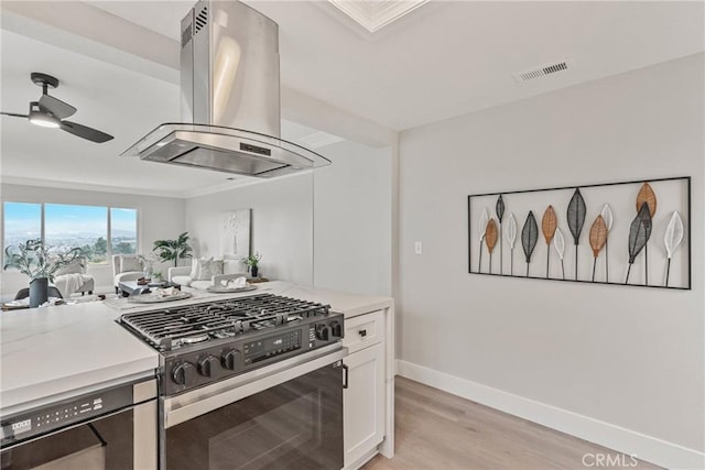 kitchen featuring light hardwood / wood-style flooring, ceiling fan, range with gas stovetop, white cabinets, and island exhaust hood