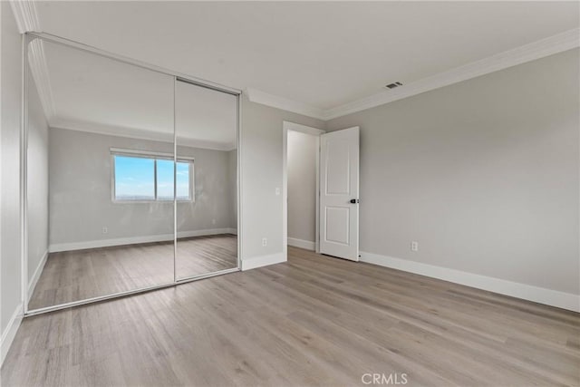 unfurnished bedroom featuring crown molding, a closet, and light hardwood / wood-style flooring