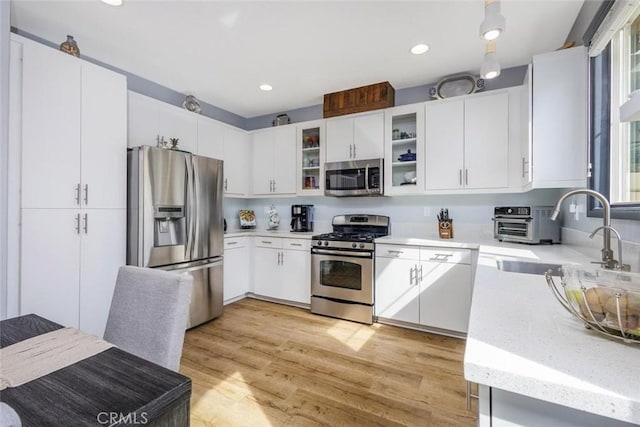 kitchen with stainless steel appliances, sink, white cabinets, and light hardwood / wood-style flooring