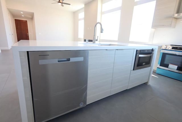 kitchen with sink, stainless steel appliances, ceiling fan, and dark tile patterned flooring