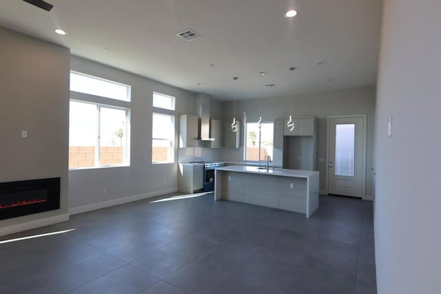 kitchen with hanging light fixtures, a kitchen island, wall chimney range hood, and stainless steel range with electric cooktop