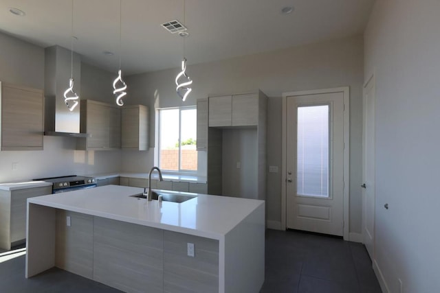 kitchen featuring stainless steel electric stove, pendant lighting, sink, a kitchen island with sink, and wall chimney range hood