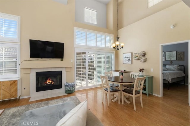 dining space featuring hardwood / wood-style floors, a notable chandelier, a fireplace, and a towering ceiling