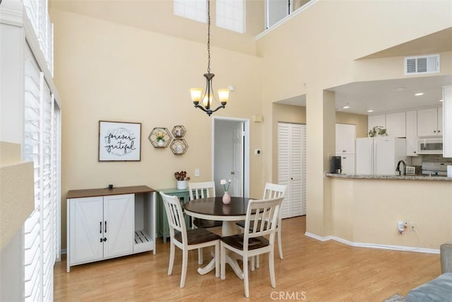 dining area featuring a towering ceiling, sink, an inviting chandelier, and light hardwood / wood-style flooring