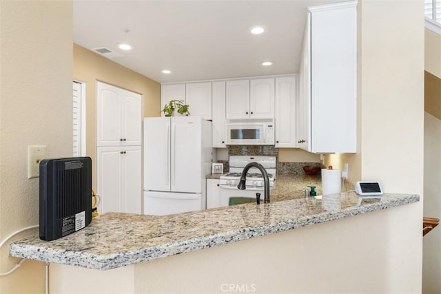 kitchen with white cabinetry, light stone counters, white appliances, and kitchen peninsula