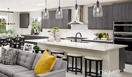 kitchen with a kitchen island with sink, wall chimney range hood, sink, and hanging light fixtures