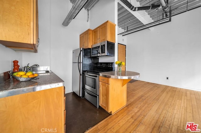 kitchen featuring hardwood / wood-style floors, appliances with stainless steel finishes, a breakfast bar, and sink