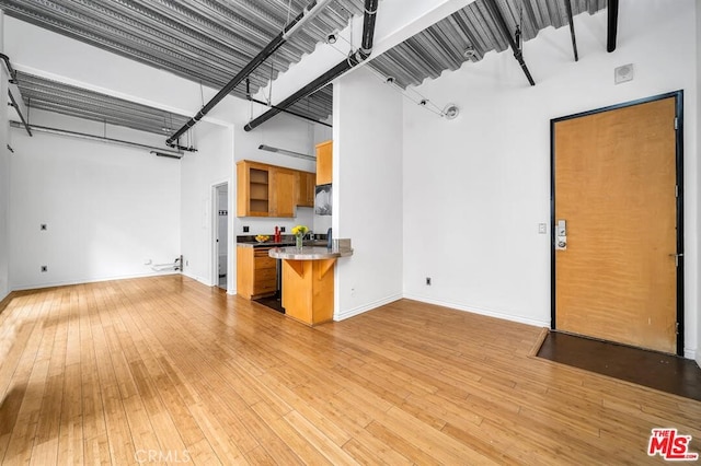 unfurnished living room featuring light wood finished floors, a high ceiling, and baseboards