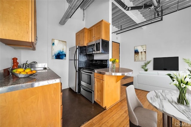 kitchen featuring sink, light hardwood / wood-style flooring, a breakfast bar area, appliances with stainless steel finishes, and a towering ceiling