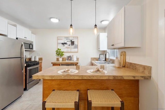 kitchen featuring appliances with stainless steel finishes, white cabinetry, a kitchen breakfast bar, decorative light fixtures, and kitchen peninsula