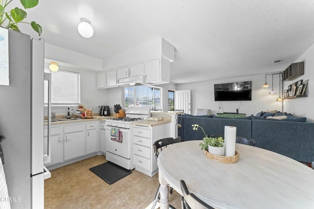 kitchen featuring white cabinets, light countertops, freestanding refrigerator, a peninsula, and white gas range oven
