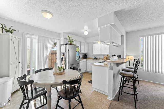kitchen featuring a wealth of natural light, freestanding refrigerator, white dishwasher, and a peninsula