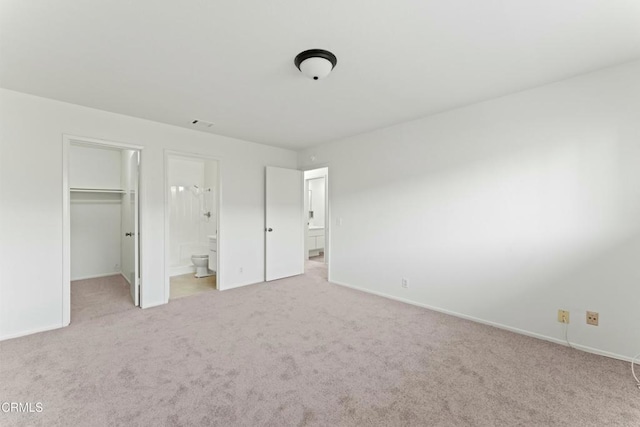 unfurnished bedroom with connected bathroom, a closet, carpet floors, a walk in closet, and baseboards