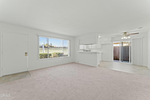unfurnished living room featuring ceiling fan, light colored carpet, visible vents, and a healthy amount of sunlight