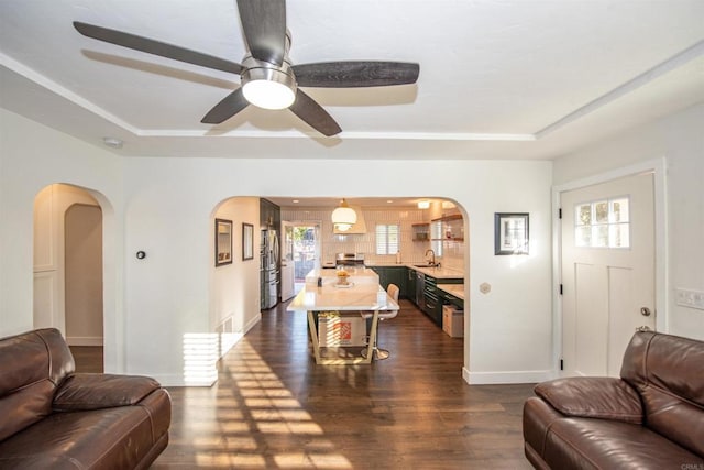 living room with a raised ceiling, dark hardwood / wood-style floors, sink, and ceiling fan