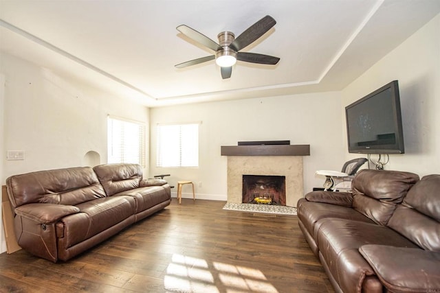 living room featuring dark hardwood / wood-style floors, ceiling fan, a high end fireplace, and a tray ceiling