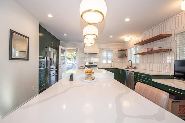 kitchen featuring sink, appliances with stainless steel finishes, green cabinets, hanging light fixtures, and light stone counters