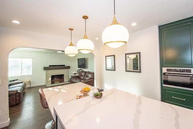 kitchen featuring oven, dark hardwood / wood-style flooring, hanging light fixtures, light stone counters, and green cabinetry