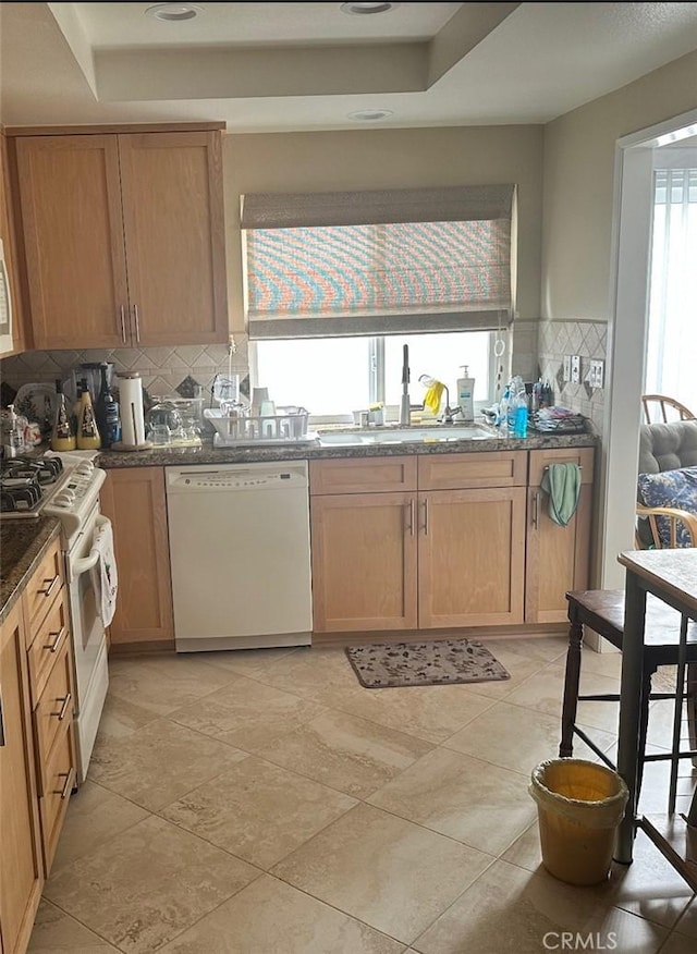 kitchen with tasteful backsplash, white appliances, a tray ceiling, and dark stone countertops