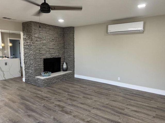 unfurnished living room featuring hardwood / wood-style flooring, a stone fireplace, a wall mounted AC, and ceiling fan