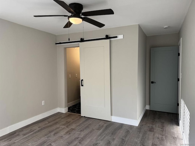 unfurnished bedroom featuring hardwood / wood-style flooring, a barn door, and ceiling fan