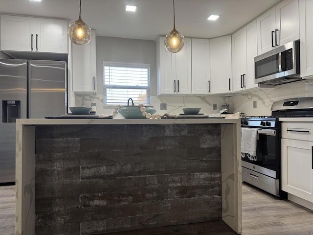 kitchen featuring stainless steel appliances, hanging light fixtures, white cabinets, and decorative backsplash