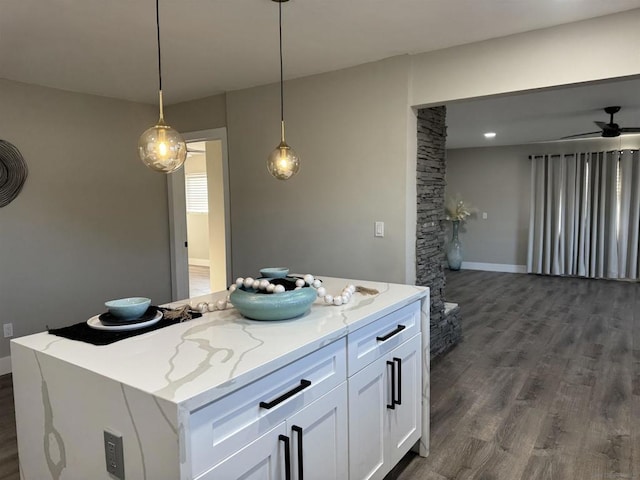 kitchen featuring a kitchen island, white cabinetry, hanging light fixtures, light stone countertops, and dark wood-type flooring