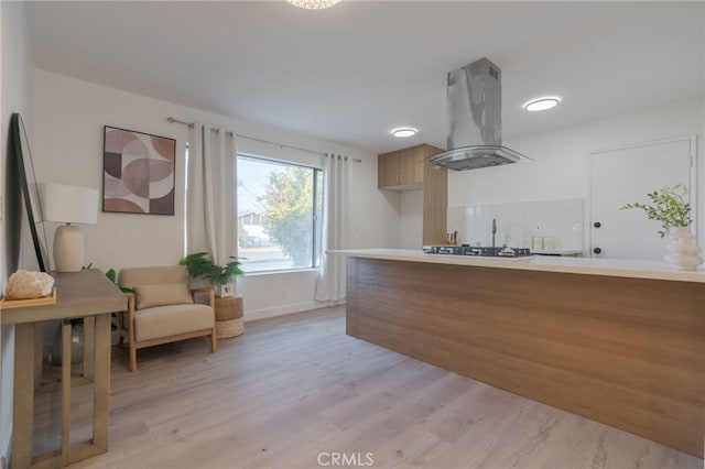 kitchen with baseboards, island range hood, light countertops, light wood-style floors, and stainless steel gas cooktop